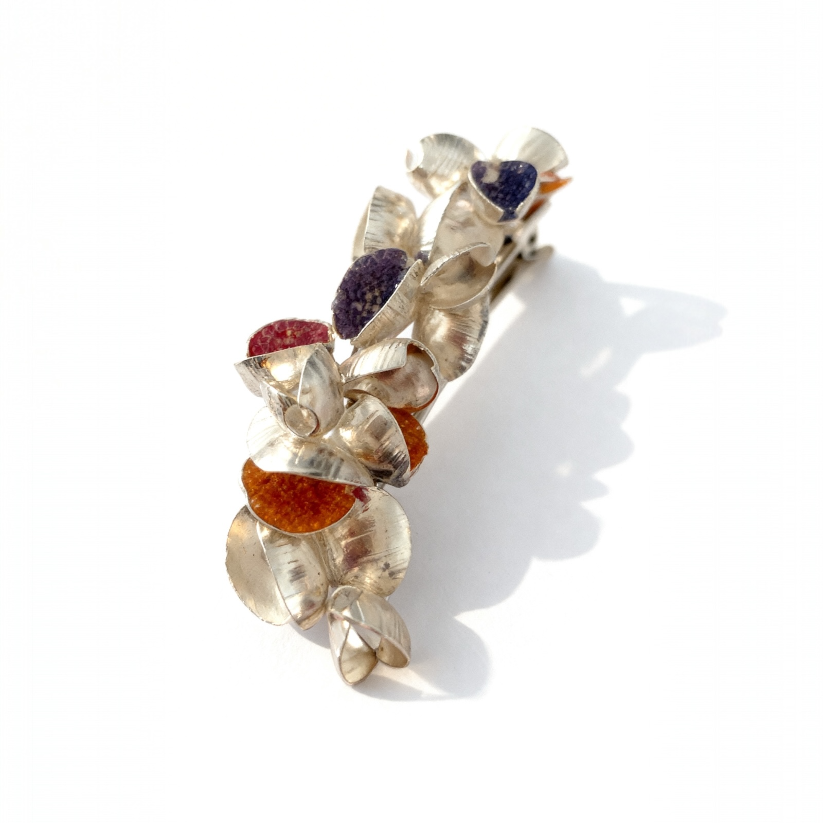 Handcrafted silver brooch with textured petals and orange, purple accents on white background